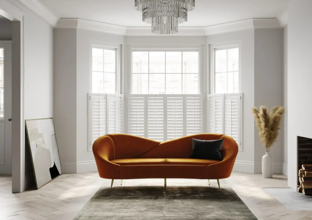 Café style plantation shutters on a bay window behind a velvet sofa